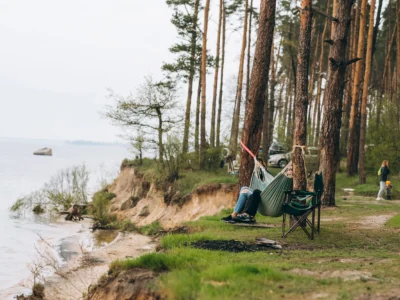 Zwei Personen genießen eine ruhige Auszeit in einer Hängematte an einem Waldrand mit Blick auf einen See.