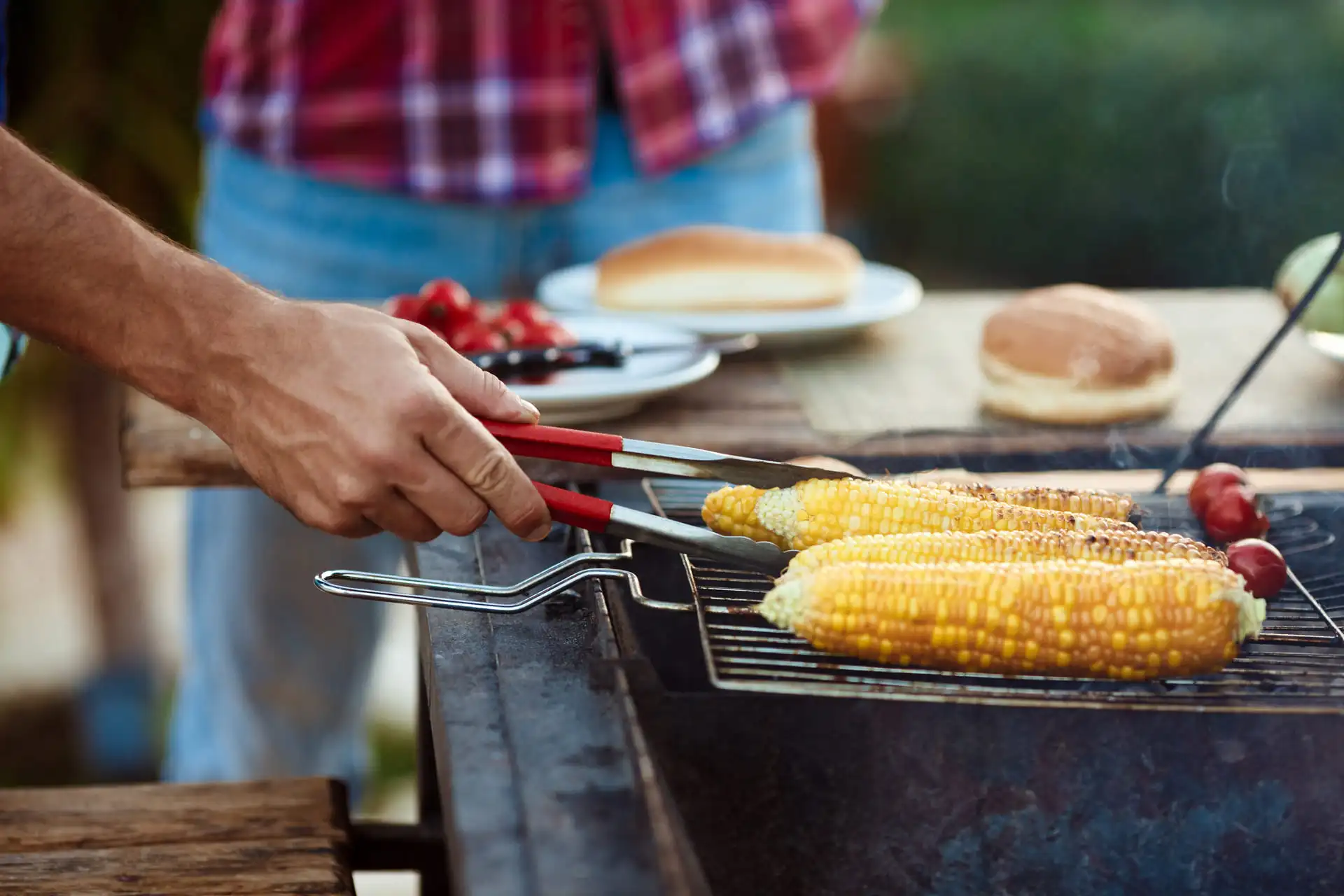 Goldbraun geröstete Maiskolben auf dem Grill mit Beilagen im Hintergrund