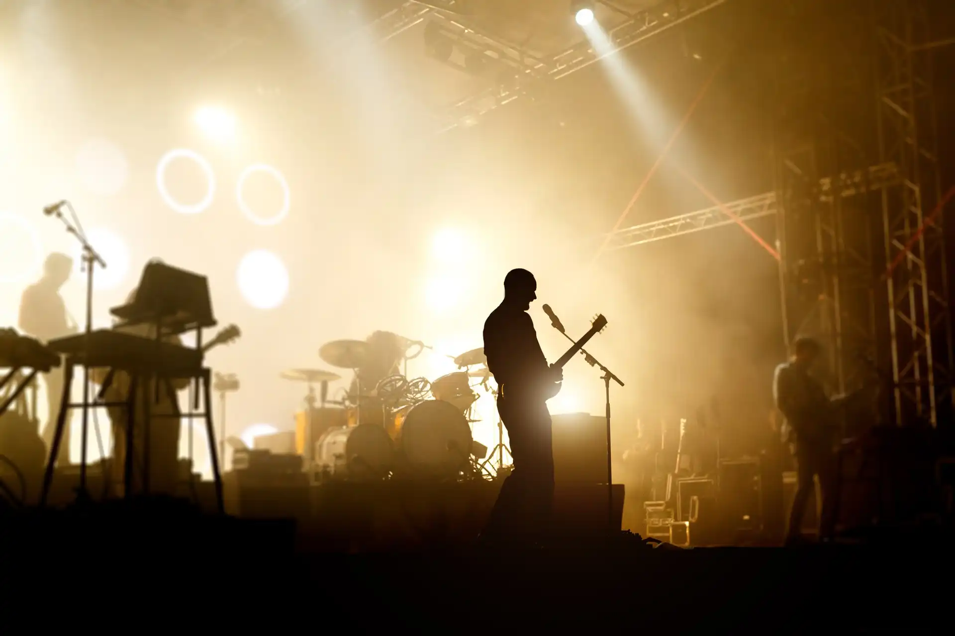 Ein Mitglied einer Rockband spielt Gitarre auf einer Bühne, die von leuchtend gelben Scheinwerfern beleuchtet wird. Die energiegeladene Szene könnte einen Auftritt im Rahmen des "Rock am Ring 2025 Lineup" darstellen.